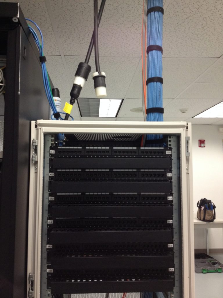 In a larger server room, a network rack cleanup service dressed the network cables that fall in a straight line out of the ceiling. the rack is very clean and neat.